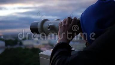 一个年轻人手里拿着望远镜，在日落时看城市的全景。慢动作。1920x1080。满的